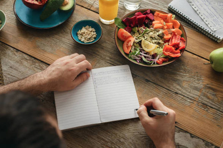 サラダを食べながらノートを書く女性の写真